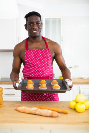 Man in apron holding baking sheet with cupcakesの写真素材