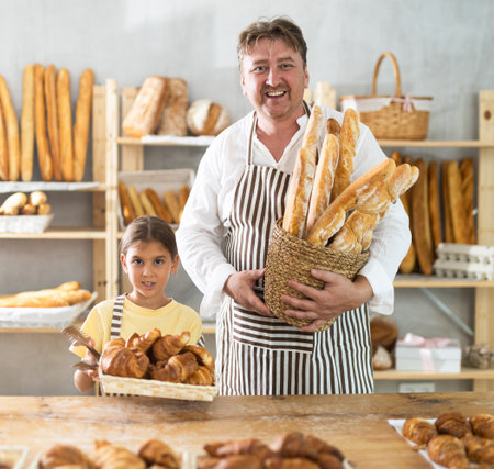 Bakery employees, father and daughter, offering bread, croissant and various baguettes for saleの写真素材