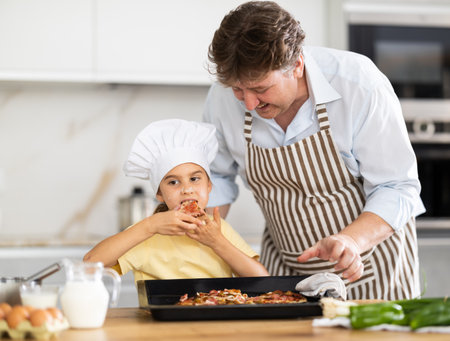 Daughter eats pizza prepared by fatherの写真素材