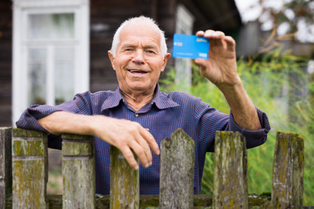 Old man with credit card standing beside his houseの写真素材