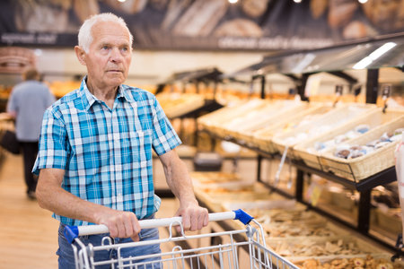 old age senor examines bakery products in the grocery section of the supermarketの写真素材