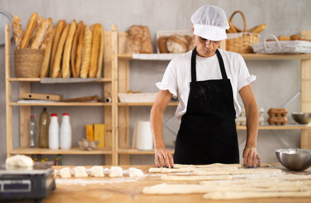 Female baker rolls dough into long sausages to be cut into pieces for baking buns