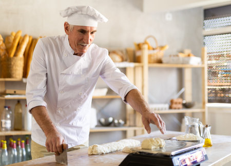Mature experienced baker weighs pieces of raw dough on scales for making croissants