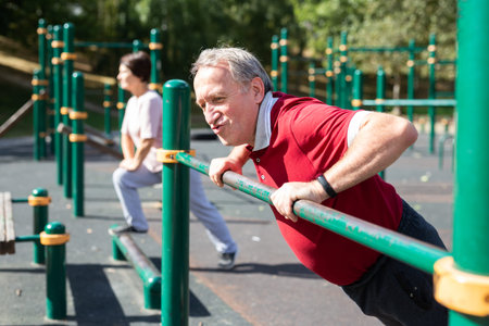 Elderly athletic man doing push-ups from the crossbar on outdoor sports ground