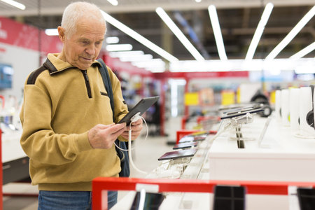 elderly man examines tablet computer in showroom of electronics storeの写真素材