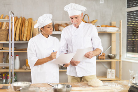 Two experienced bakers read new recipe on paper, discussing a method for making delicious bread