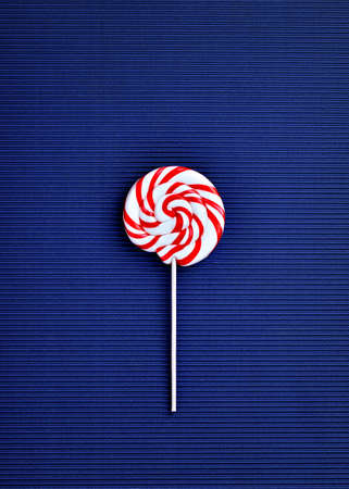 Delicious red striped and spiral shaped lollypop on dark blue horizontal striped backgroundの写真素材
