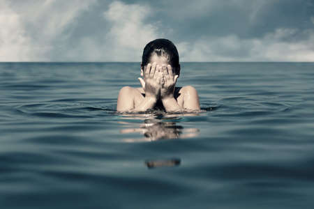 Caucasian little boy covers his face with his hands in the sea. Concept of child abuse, depression,...
