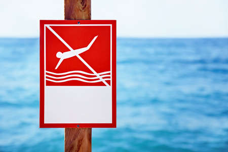 Closeup red no diving sign with copy space nailed to a  a wooden plank in front of a blurry wavy blue sea backgroundの写真素材