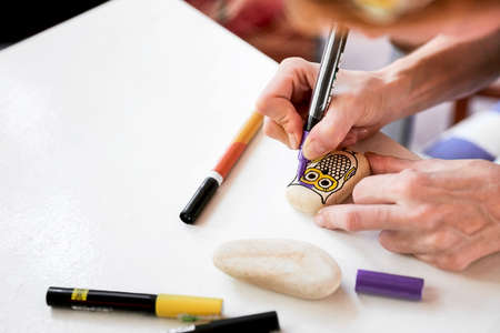 Caucasian woman painting an owl on a stone. Stone paint hobby, arts and crafts.の写真素材