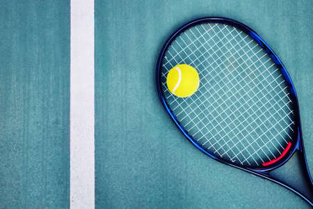 Top down view of a tennis racket, a single ball and the white line on a cyan concrete tennis court
