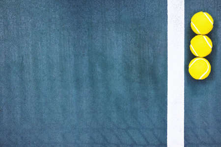 Top down view of three yellow tennis balls near the line on blue concrete tennis court with copy...