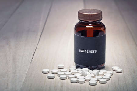 Concept of anti-depressant drug use and happiness. A drug container with black label written happiness on it. White pill tablets in the front. Room for copy space text.の写真素材