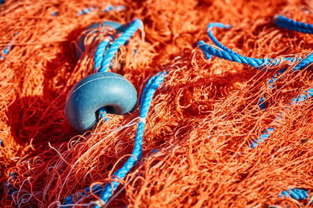 Orange colorful fishing net with blue rope and float on the dock. Close up.