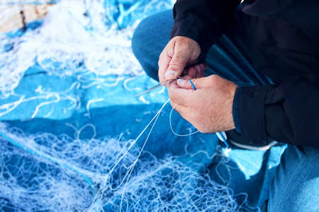 Hands of a fisherman repairing a fishing net using a knife and net needle