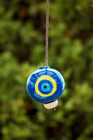 Decorative ceramic evil eye bead hanging in front of a blurry green plant background.