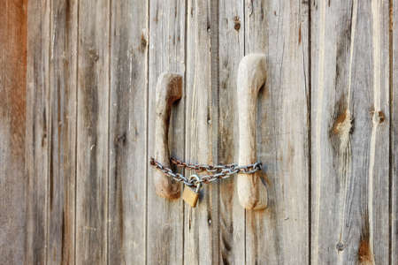 Close up view of an old wooden barn door locked with rusty chain and padlock