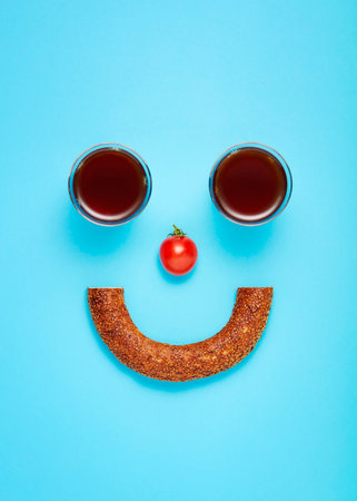 Turkish bagel (simit) tea glasses and a cherry tomato designed as a smiley face. Concept of light and healthy diet breakfast.の写真素材