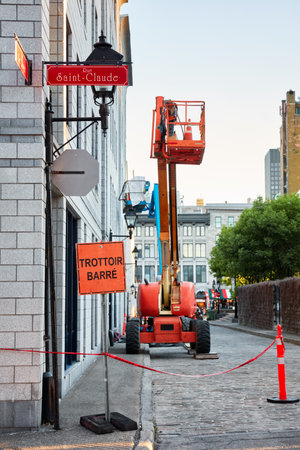 Montreal, Canada - June, 2018: Work lift truck executes construction maintenance on Rue le Royer street and pavement closed (trottoir barre) sign in Montreal, Quebec, Canada. Editorial use.のeditorial素材
