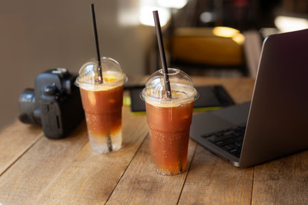 Iced coffee in plastic cups with laptop and camera on wooden table