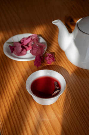 tea in a white cup on a wooden table with rose petals