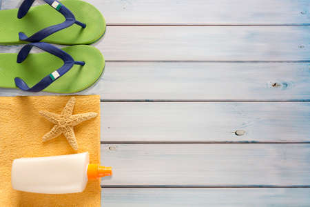 Sea slippers, sunscreen and towel on wooden background