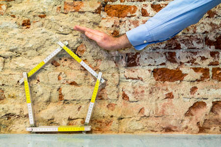 Hand protecting a house, brick wall background