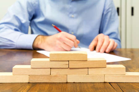 Business man and wall built with small wooden blocksの写真素材