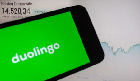 smartphone with Duolingo language app logo on screen and blurred background with Nasdaq stock index chartのeditorial素材