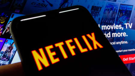 Netflix logo visible on smartphone screen, and website homepage on backgroundのeditorial素材