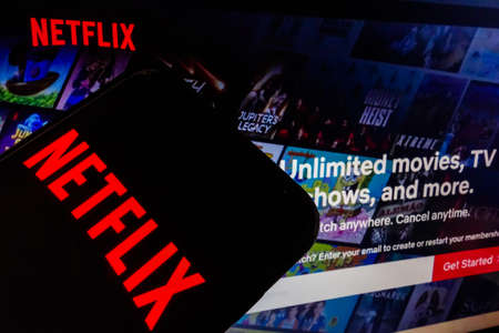 Netflix logo visible on smartphone screen, and website homepage on backgroundのeditorial素材