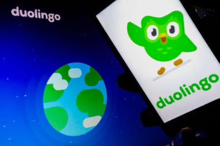 smartphone with Duolingo language app logo on screen. Blurred background with Duolingo websiteのeditorial素材