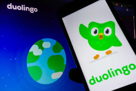 smartphone with Duolingo language app logo on screen. Blurred background with Duolingo websiteのeditorial素材