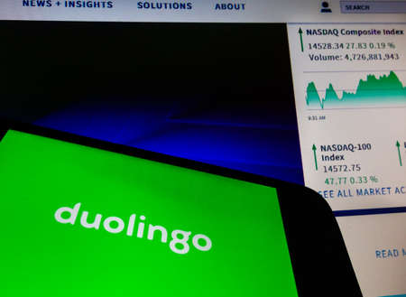 smartphone with Duolingo language app logo on screen and blurred background with Nasdaq stock index chartのeditorial素材