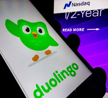 smartphone with Duolingo language app logo on screen and blurred background with Nasdaq stock index chartのeditorial素材