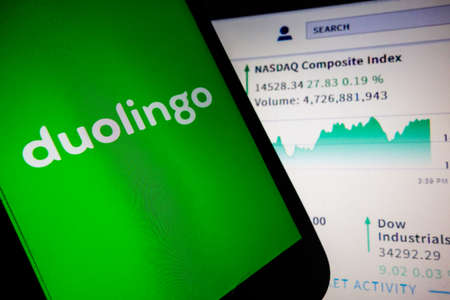 smartphone with Duolingo language app logo on screen and blurred background with Nasdaq stock index chartのeditorial素材