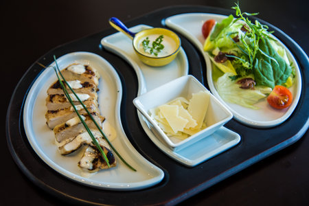Grilled chicken breast with salad and cheese on white plate in restaurant,  Food Fotography art shots, Photos is selective focus with shallow depth of field. goat cheese wheelの写真素材