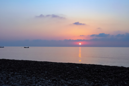 Pastel sunrise on Cirali Beach: Pastel hued sunrise with boats bobbing in ethereal flat waveless water seen from pebble beach in Cirali, Turkey.の写真素材