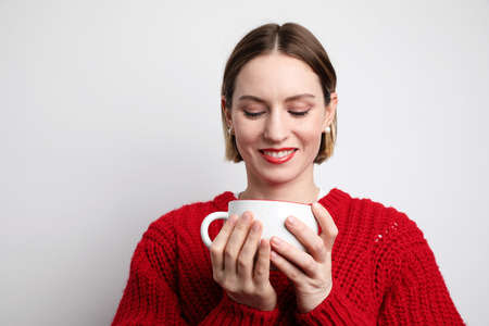 Young woman wearing casual clothing and drinking hot coffee. Studio background.
