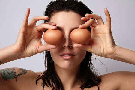 Close-up portrait of young woman posing on white wall with two eggs. High quality photo