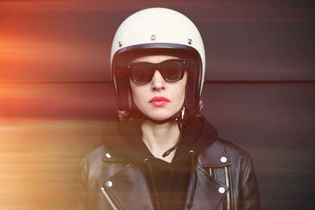 Close-up portrait of biker girl wearing sunglasses and white helmet. Dark background.