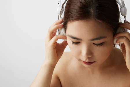 Side portrait of Chinese woman posing on the white background with big earphones. Isolated.の写真素材