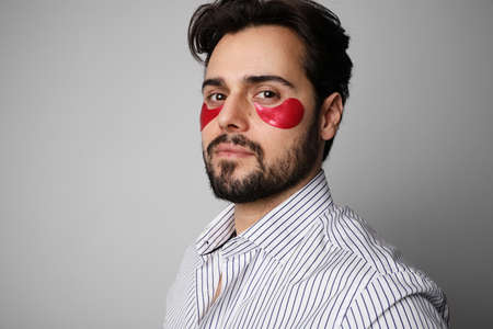 Portrait of young bearded man using hydrating red patches. Space for text.の写真素材