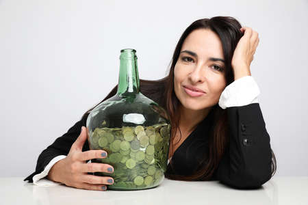 Portrait of a cheerful young woman holding a big bottle with money. Isolated.の写真素材