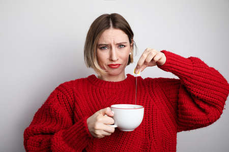 Young woman with negative face showing tea bagging in her cup. Isolated.