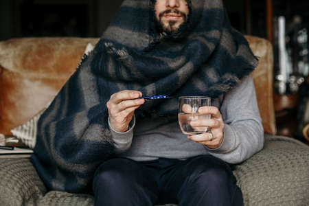 Bearded hipster man having virus. Taking medicine in the house.の写真素材