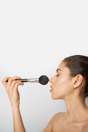Young woman doing make-up with a big brooch. Vertical.