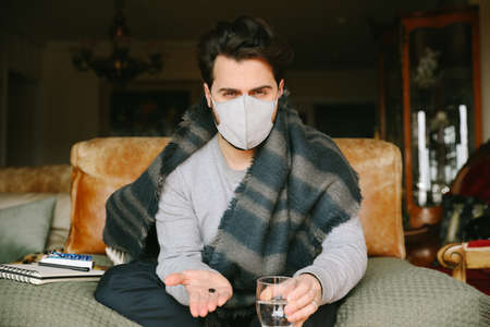 Close-up portrait of young bearded man get a virus and using a medical mask. Quarantine at home.