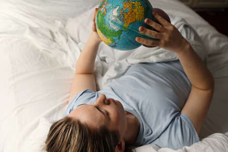 Close-up portrait of young woman laying in bed and holding globe. Horizontal.