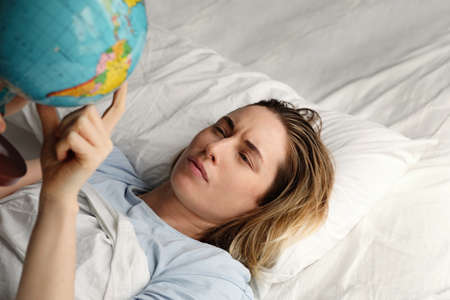 Close-up portrait of young woman laying in bed and holding globe. Horizontal.